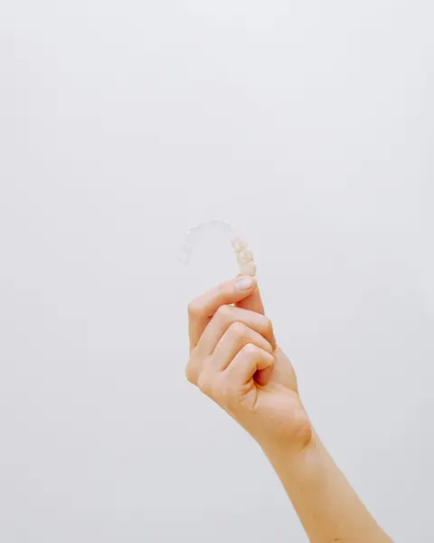 A hand holding a clear removable aligner tray up against a white wall.